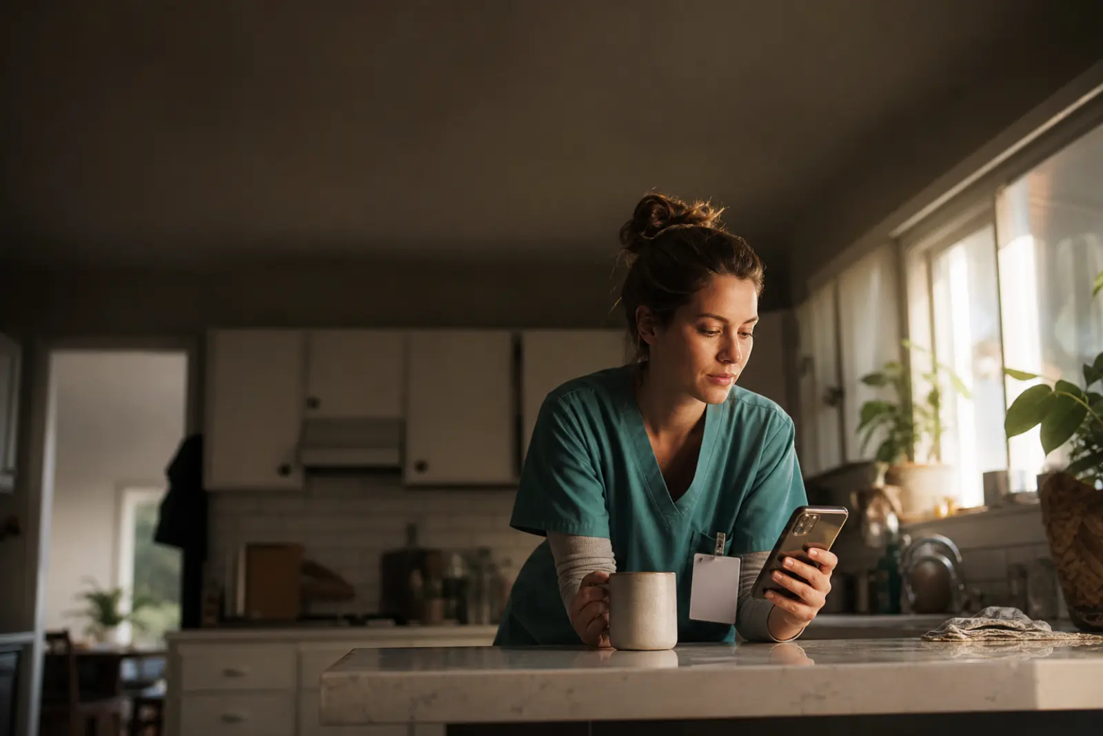 A clinician in teal scrubs reading her phone over coffee before a shift